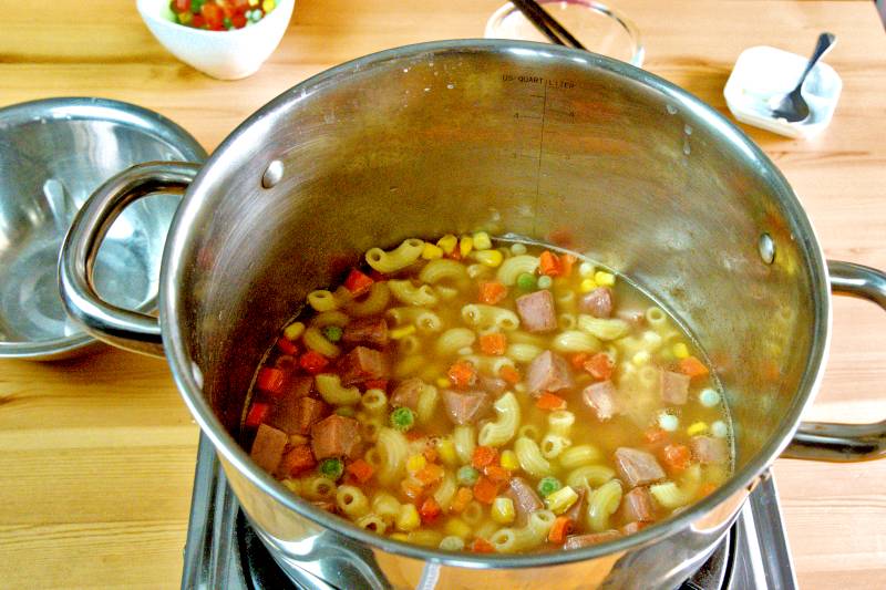 Add the mixed vegetables, the cubes of luncheon meat, and the cooked pasta to the hot soup. 